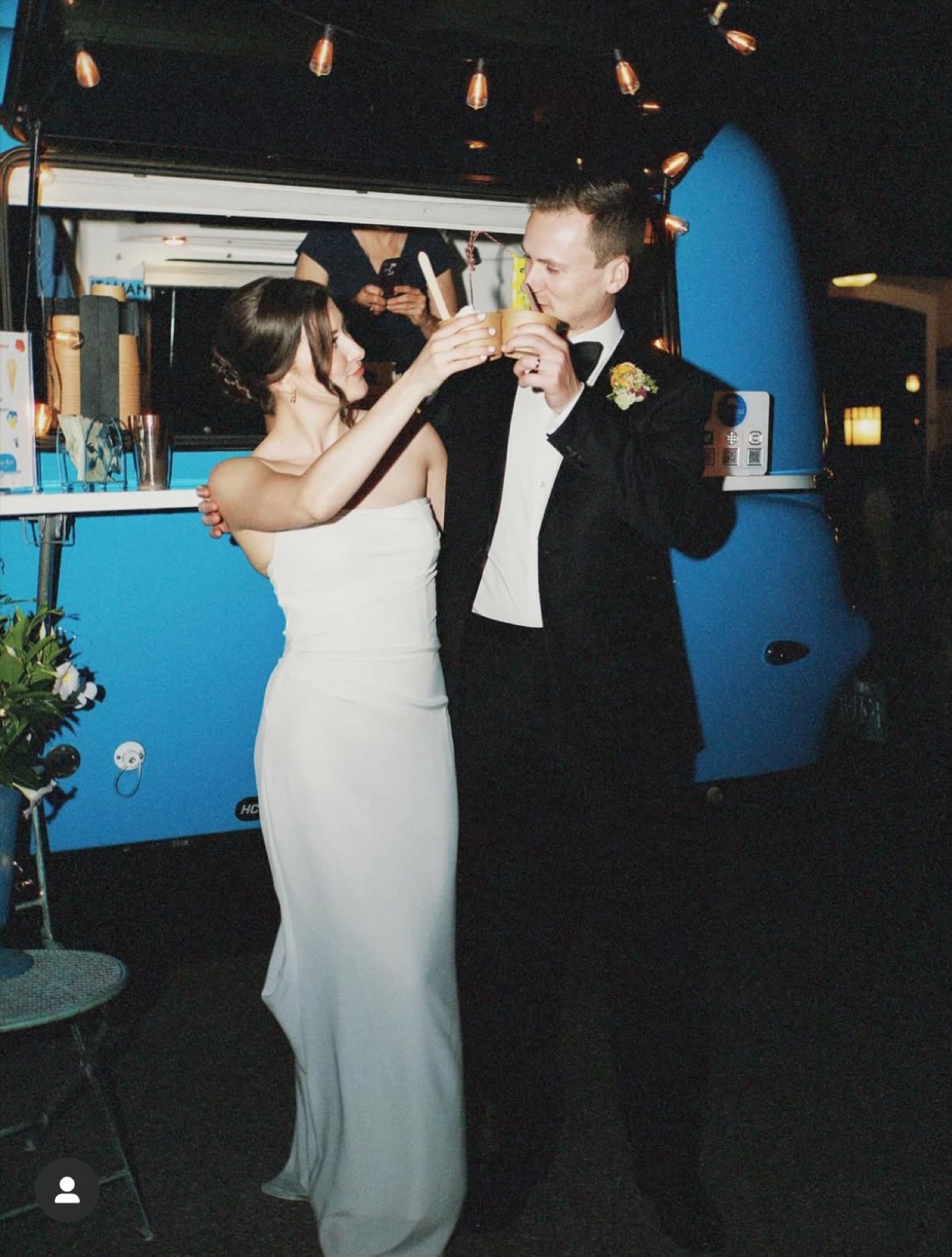 Bride and groom toasting with espresso drinks in front of the Blue Bird camper at night