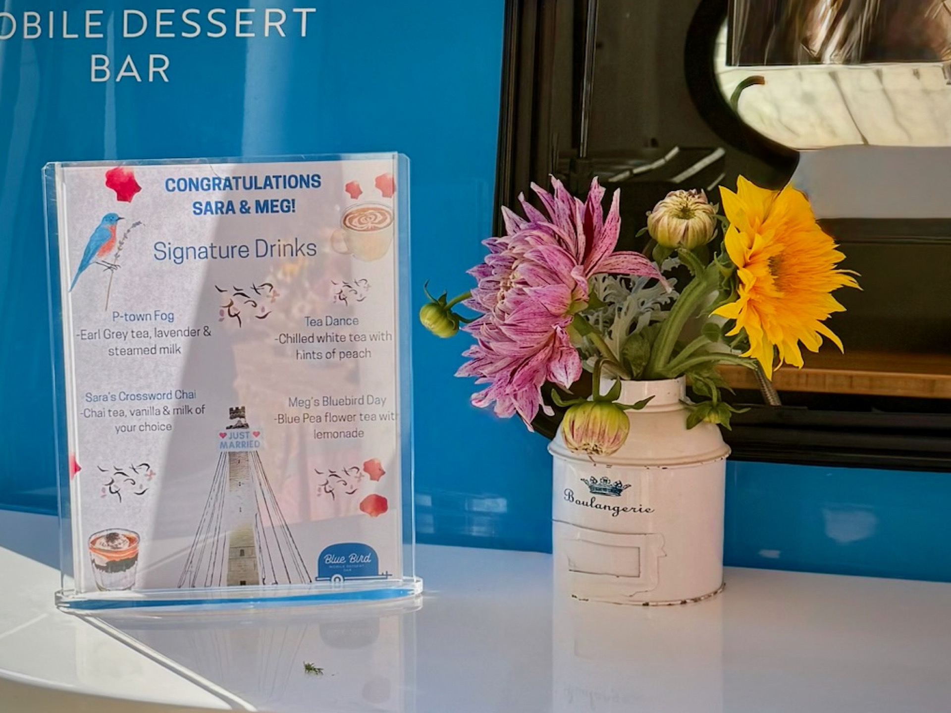 Signature drinks menu for Sara and Meg's Provincetown wedding, displayed beside fresh flowers on the Blue Bird camper counter